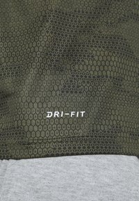 Zelená vzorovaná Dri-Fit tkanina má hexagonální design s hladkým povrchem; spodní část je šedá, což vytváří barevný kontrast.