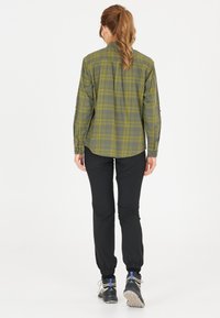 Grön och gul rutig skjorta med knappmanschetter, tillsammans med svarta avsmalnande byxor och grå skor. Mjuk tyg, avslappnad passform och klassisk design.