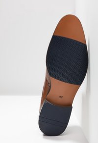 Semelle de chaussure habillée en cuir marron avec des patchs en caoutchouc noir pour l'adhérence et la taille 42 imprimée près du talon.