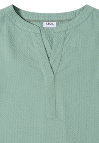 Blouse vert clair texturée avec un col rond et une fente en V à l'avant, étiquetée "Cecil" à l'intérieur du col.