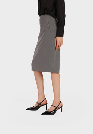 Donna che indossa una gonna aderente grigia al ginocchio, una blusa nera a maniche lunghe e décolleté slingback nere in vernice con punta appuntita.