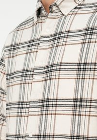 Βαμβακερό πουκάμισο κοντομάνικο με καρό σχέδιο σε μπεζ, μαύρο και καφέ. Διαθέτει γιακά με κουμπιά και κουμπιά μπροστά.