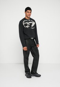 Fekete pulóver kontrasztos krémszínű grafikával, fekete bőr cargo nadrággal és fekete texturált cipővel párosítva. Minimalista dizájnelemek.