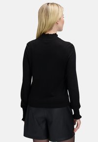 Zwarte trui met lange mouwen en een gerimpelde kraag, gemaakt van een textuurmateriaal. Draag het met hoge taille shorts, wat een strakke silhouet laat zien.