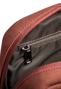 Borsa in tessuto marrone con chiusura a cerniera liscia. L'interno presenta una fodera nera testurizzata. Il tirazip è metallico con una piccola fessura.