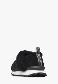 Sneaker nera caratterizzata da un mix di suede e texture soffici, una suola bianca e un'etichetta del tallone con logo. Forma curva con dettagli morbidi e ammortizzanti.