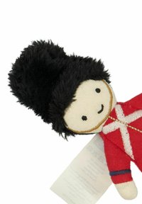 Měkká textilní hračka připomínající britského vojáka, s červeným uniformou s bílými akcenty a černou chlupatou čepicí. Jednoduché rysy obličeje.