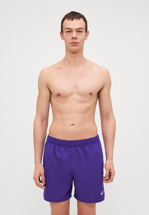 Lila fürdőnadrág rugalmas derékkal és fehér Nike logóval. Egyszerű fehér háttéren, kiegészítők nélkül elhelyezve.