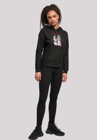 Sudadera negra con un estampado gráfico en la parte frontal, que incluye un bolsillo delantero, combinada con leggins negros y zapatillas. Tejido de mezcla de algodón suave.
