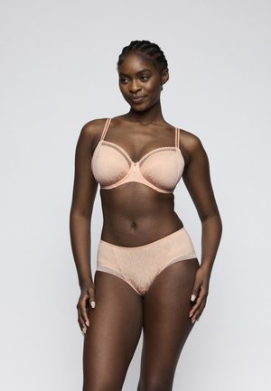 Woman with braided hair posing in light pink matching bra and high-waist underwear against plain gray background.
