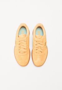 Zapatillas con un suave exterior de ante naranja, diseño de cordones, cuello acolchado y plantilla azul claro. Suela de goma con patrones sutiles.