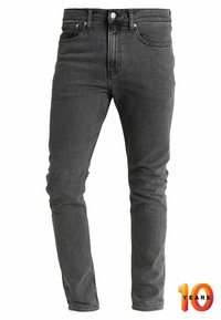 Vaqueros de denim negro con un corte ajustado, que cuentan con cinco bolsillos, una cremallera y una textura sutil. Incluye un gráfico conmemorativo "10 Años".