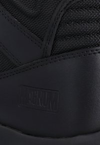 Close-up of black Magnum boot with textured fabric and smooth leather sections, showing embossed Magnum logo on the side.