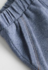 Des shorts en tissu gris présentent une taille élastique froncée et des coutures contrastantes orange, mettant en valeur un aspect doux et texturé.
