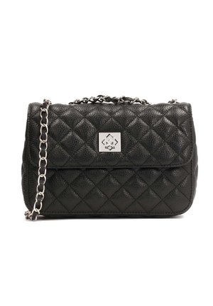 Personne portant une veste en jean blanche et un jean avec une ceinture noire, un crop top noir, des bottines noires et tenant un petit sac matelassé noir.