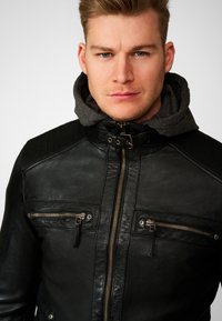 Schwarze Lederjacke mit grauem Kapuzenpullover, ausgestattet mit gerippten Schulterakzenten, zwei Reißverschlusstaschen auf der Brust und einem Reißverschluss vorne.