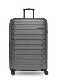 Grande valise rigide grise avec des rayures horizontales, quatre roues pivotantes et une poignée télescopique extensible.