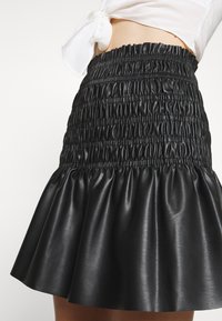 Jupe en simili cuir noir avec un waistband froncé et un ourlet évasé et froncé. La texture est lisse avec une finition légèrement brillante.