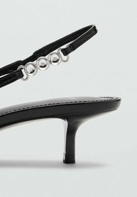 Černé sandály na vysokém podpatku s elegantním designem, s lesklým povrchem, tenkým páskem a třemi kovovými akcenty na přední straně.