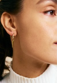 Orecchino a cerchio d'oro con un pendente triangolare e appuntito. L'orecchino presenta una fascia strutturata con piccoli accenti luccicanti. Finitura brillante e lucente.