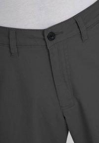 Close-up of slightly open dark gray pants waistband with black button and belt loops, worn over a light gray shirt.