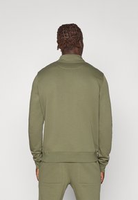 Felpa verde oliva, in tessuto leggero, con colletto allungato e polsini a costine, presenta una texture sottile e linee pulite.