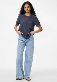 Námořnické pletené tričko s krátkým rukávem s texturovaným vzorem, v kombinaci se světle modrými širokými džíny. K outfitu patří černé ploché sandále.