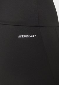 Svarta sportleggings i ett slätt, stretchigt tyg med matt yta. Utrustade med en vit "AEROREADY"-logotyp på sidan.