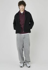 Veste noire zippée sur un polo bordeaux, associée à un pantalon large gris clair et des baskets grises. Tissu lisse avec une coupe décontractée.