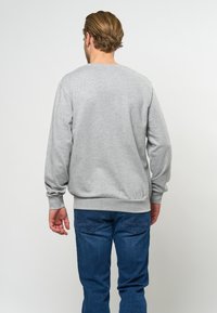 Sudadera gris de manga larga con puños acanalados, con un cuello redondo. Lleva puesto un par de jeans de mezclilla azules, visto desde la parte de atrás.