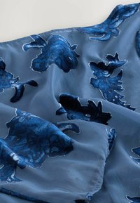 Tissu floral bleu avec texture en velours ; présente de grands motifs de fleurs bleu foncé sur une base légère bleu clair. Design doux et fluide.