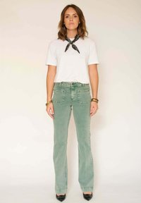 Jean vert évasé avec poches avant, associé à un t-shirt blanc et un bandana noir. Design simple, texture lisse, coupe standard.