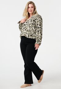 Un jean évasé noir associé à un blouse légère crème arborant un imprimé animal noir et vert, avec des manches froncées et un col en V.