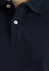 Polo shirt blu navy in tessuto testurizzato, con colletto classico, tre bottoni e un piccolo logo ricamato sul lato sinistro.