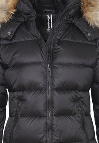 Giacca invernale nera imbottita con zip frontale completa, tasche laterali con zip e cappuccio rifinito in pelliccia, etichettata "Bomboogie."