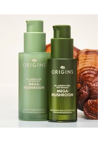 Deux bouteilles de sérums Origins Mega-Mushroom : un correcteur de taches sombres vert clair et un concentré restaurateur de la peau vert foncé, tous deux avec des pompes.