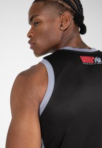 Zwarte mouwloze sporttanktop met grijze accenten en een logo op de achterkant. Het materiaal lijkt rekbaar, met een aangesloten ontwerp dat de schouders accentueert.