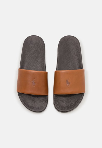 Chinelos de pele castanha com uma sola escura texturizada e uma correia larga com um logótipo em relevo. Acabamento liso sem padrões.