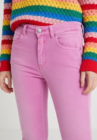 Jeans de mezclilla rosa con un ajuste slim y una textura sutil, que presentan un diseño clásico de cinco bolsillos y un botón metálico en la pretina.