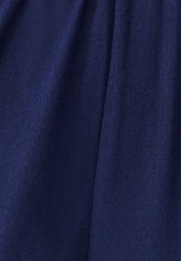 Mornarsko modra tkanina z gladko teksturo, ki kaže subtilen sijaj in rahle gubice zaradi padajoče tkanine. Brez vidnih vzorcev ali dodatkov.