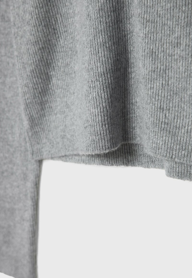 Grauer Pullover mit gerippter Textur und gerade geschnitten. Das weiche Material fällt sanft und hat einen seitlichen Schlitz für eine lockere Passform.