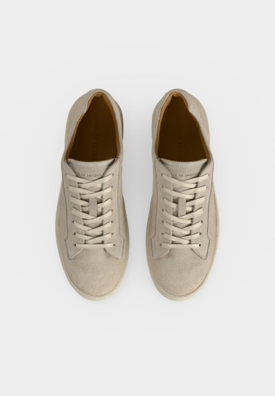 Ζευγάρι μπεζ σουέντ αθλητικά παπούτσια με κορδόνια, φωτογραφημένα από πάνω σε λευκό φόντο.