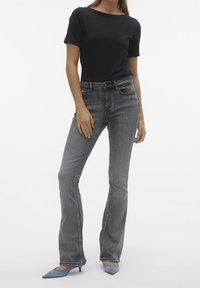 Grå utsvängda jeans med hög midja och framfickor, kombinerat med en svart åtsittande kortärmad topp och blå klackskor med spetsig tå.