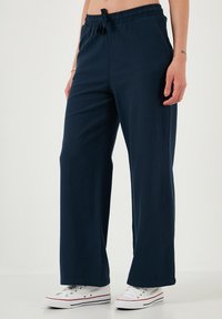 Navyblauwe wijde broek van zachte stof, met een elastische tailleband met een strik aan de voorkant en zijzakken. Gecombineerd met witte sneakers.