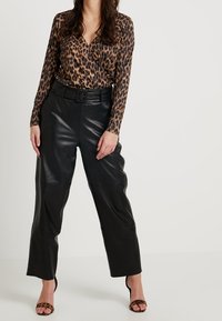 Lepelprint long-sleeve top met een v-hals en een gathered taille, gecombineerd met high-waisted zwarte leren broeken en gestrikte hakken met dierenprint.