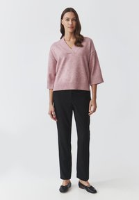 Light pink oversized sweater with a V-neck and ribbed hem, paired with black tailored pants and black slip-on shoes. Smooth texture.