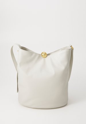 Sac à main en cuir crème en forme de seau avec un fermoir circulaire doré, une bandoulière réglable et une texture lisse, présentant un branding minimal à la base.