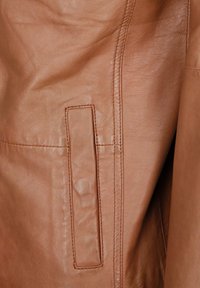 Helle Lederjacke aus Rindsleder mit glatter Textur, sichtbaren Nähten und einer rechteckigen aufgesetzten Tasche an der Seite.