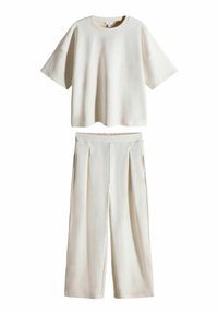 Zweiteiliges Outfit in hellem Beige, bestehend aus einem T-Shirt mit kurzen Ärmeln und weit geschnittenen Hosen. Der Stoff wirkt weich, mit einer glatten Textur und Faltendetails.