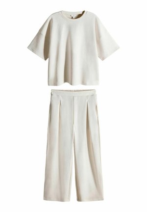 To-delt outfit i let beige, bestående af en kortærmet top og brede bukser. Stoffet ser blødt ud, med en glat tekstur og plisserede detaljer.